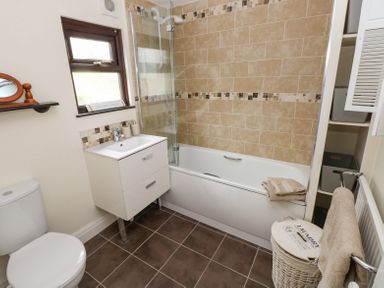 A bathroom with a toilet sink and bathtub with tiled walls and a laundry basket at Dunnock Cottage in Broad Haven