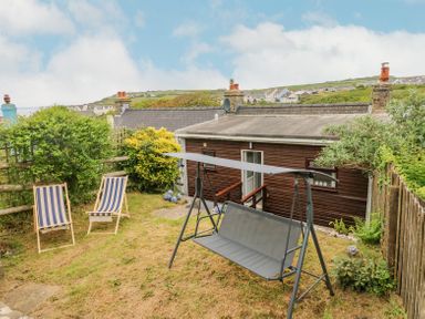 A garden with two striped deck chairs and a gray swing near a wooden building at Dunnock Cottage in Broad Haven