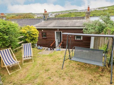 A garden with two striped deck chairs a swing and a wooden house in the background at Dunnock Cottage in Broad Haven