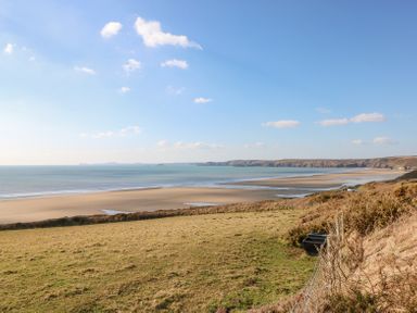 A coastal landscape with a sandy beach grass fields and ocean at Dunnock Cottage in Broad Haven