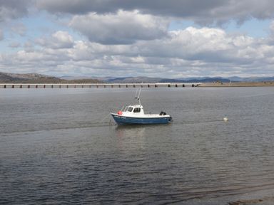 A small boat named north star floating on a body of water with a long bridge and mountains in the background at Lavender Cottage in Cark In Cartmel