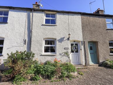 Exterior view of a white terraced house with flower garden and a door with a wreath at Lavender Cottage in Cark In Cartmel
