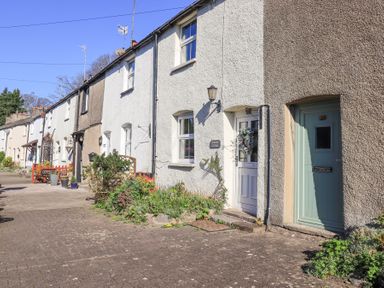 A row of connected cottages with doors and windows along a paved walkway at Lavender Cottage in Cark In Cartmel