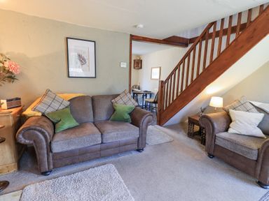 A living room with brown sofas and wooden stairs at Lavender Cottage in Cark In Cartmel
