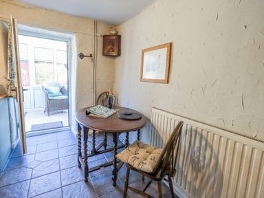A small dining area with a round wooden table and two chairs near a door leading to a porch at Lavender Cottage in Cark In Cartmel