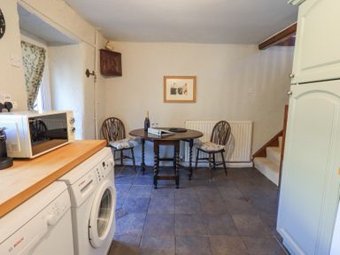 A kitchen with washing machine dishwasher microwave and a wooden table with two chairs at Lavender Cottage in Cark In Cartmel