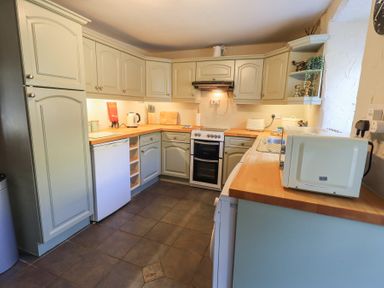 A kitchen with cabinets appliances including a stove microwave toaster and kettle at Lavender Cottage in Cark In Cartmel
