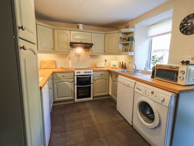 A kitchen with cabinets appliances a window and a clock at Lavender Cottage in Cark In Cartmel