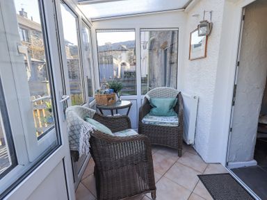 A sunroom with two wicker armchairs a small round table and a basket in Lavender Cottage in Cark In Cartmel