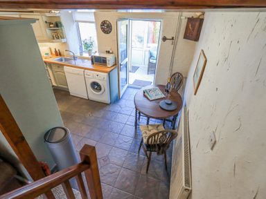 A kitchen area with a round wooden table and two chairs a dishwasher washing machine microwave and sink visible at Lavender Cottage in Cark In Cartmel