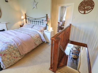 A bedroom with a patterned bedspread next to carpeted stairs and a small table with chairs downstairs at Lavender Cottage in Cark In Cartmel