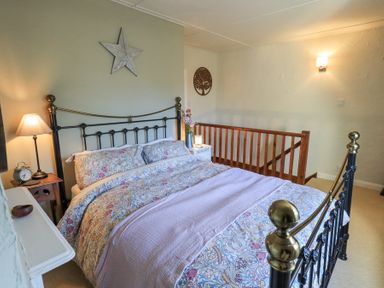 A bedroom with a metal bed frame floral bedding bedside tables and lamps at Lavender Cottage in Cark In Cartmel