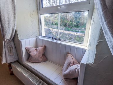 A window seat with two pillows and three bird figurines on the windowsill at Lavender Cottage in Cark In Cartmel