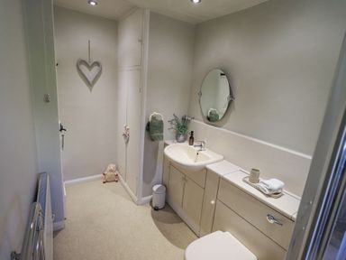 A bathroom with a sink, mirror, toilet, cabinets, towel holder, and heart decoration on the wall at Lavender Cottage in Cark In Cartmel