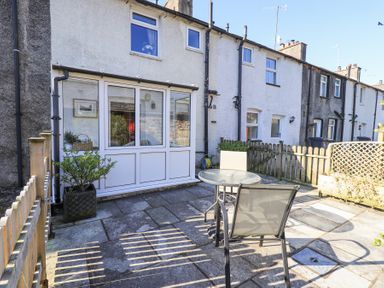 A patio area with a glass table and chair in front of a row of terrace houses at Lavender Cottage in Cark In Cartmel