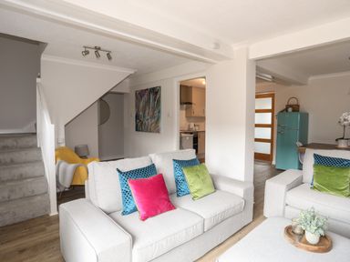 A living room with two gray sofas and colorful cushions next to a kitchen and a staircase at 240 Cae Du in Abersoch