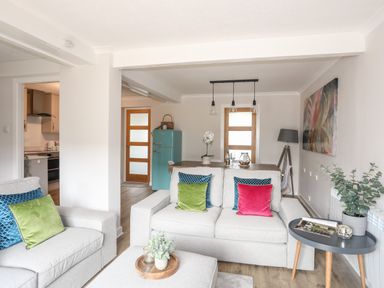 A living room and dining area with beige sofas, colorful cushions, a wooden dining table, a turquoise fridge, and a side table with plants at 240 Cae Du in Abersoch
