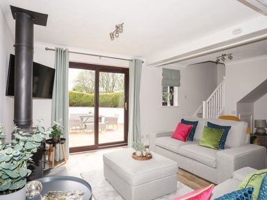 A living room with grey sofas and colorful cushions next to sliding glass doors opening to a patio at 240 Cae Du in Abersoch