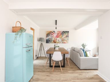 A dining area with a wooden table and white chairs next to a living room with a gray sofa and a blue refrigerator at 240 Cae Du in Abersoch