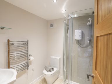 A bathroom with a toilet with folded towels a glass shower enclosure a chrome towel radiator and a wooden door at 240 Cae Du in Abersoch