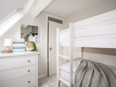 A bedroom with a white bunk bed and a white dresser with a lamp plant and decorative signs at 240 Cae Du in Abersoch