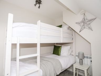 A bedroom with a white bunk bed green pillows gray blanket a small white side table with a gray lamp and a star decoration on the wall at 240 Cae Du in Abersoch