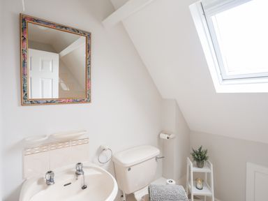 A bathroom with a sink mirror toilet with towel and a small shelf with plant and candle at 240 Cae Du in Abersoch