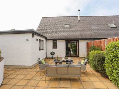 An outdoor patio with wicker furniture and a small barbecue grill at 240 Cae Du in Abersoch