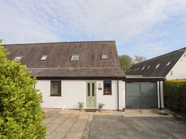 A white house with a green door two potted plants and a grey garage door at 240 Cae Du in Abersoch