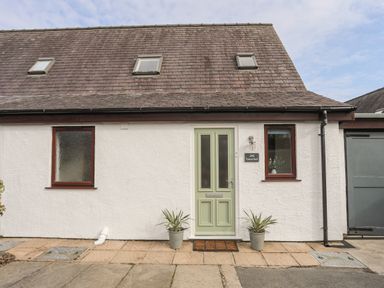 The front exterior of a house with a light green door two windows and two potted plants at 240 Cae Du in Abersoch