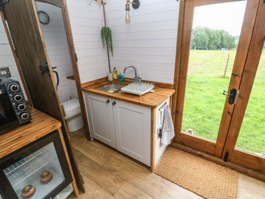 A kitchen area with a sink dishwasher rack and cleaning supplies next to wooden framed glass doors overlooking a grassy field at Fern in Broad Langdon near Wainhouse Corner