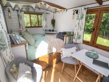 A small room with a bed, two gray chairs, a white table, books, and windows with curtains at Fern Broad Langdon near Wainhouse Corner
