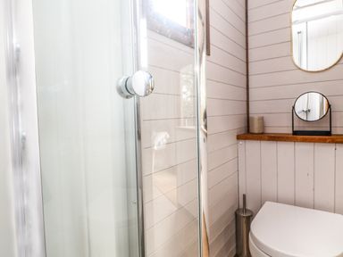 A bathroom with a toilet a shower with glass door a small round mirror and a wooden shelf at Fern Broad Langdon near Wainhouse Corner