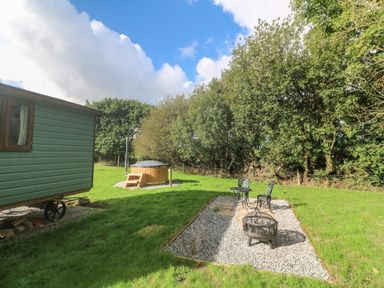 A garden with a green wooden wagon a wooden hot tub and a seating area with metal chairs and a fire pit at Fern Broad Langdon near Wainhouse Corner