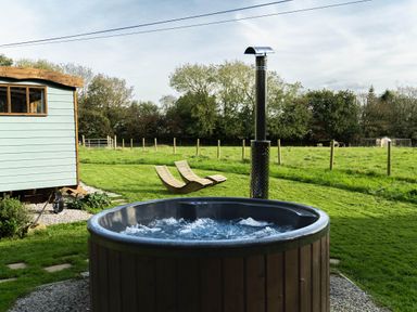 An outdoor area with a wooden hot tub bubbling on gravel two lounge chairs on grass and a light blue wooden shed at Fern Broad Langdon near Wainhouse Corner
