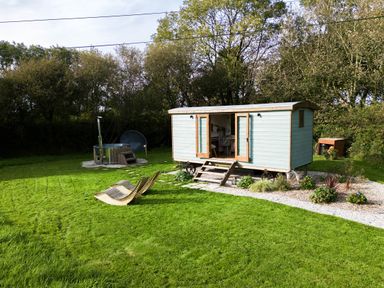 A small wooden cabin with open doors a hot tub and two wooden lounge chairs on a grassy lawn at Fern Broad Langdon near Wainhouse Corner