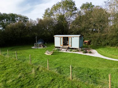 A small wooden cabin with open doors on a grassy area near a hot tub and lounge chair at Fern Broad Langdon near Wainhouse Corner