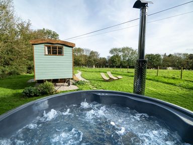An outdoor bubbling hot tub with a wood chimney and a small green cabin and two wooden lounge chairs on grass at Fern in Broad Langdon near Wainhouse Corner