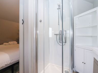 A bathroom with a glass shower enclosure and white storage cabinet next to a bedroom at Duck Lodge in Bedale