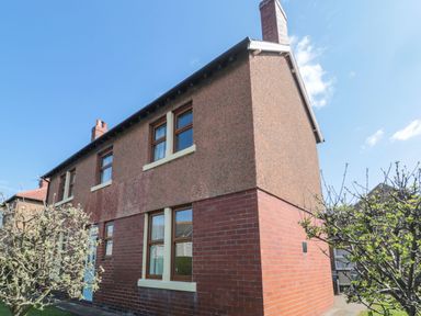 An exterior view of a two-story house with brick and pebble dash walls and windows surrounded by small trees at Bisley House in Amble