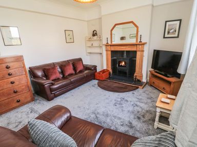 A living room with leather sofas a fireplace a wooden chest of drawers a television on a wooden stand and framed pictures at Bisley House in Amble