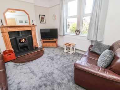 A living room with a fireplace a television a brown leather sofa and a window at Bisley House in Amble