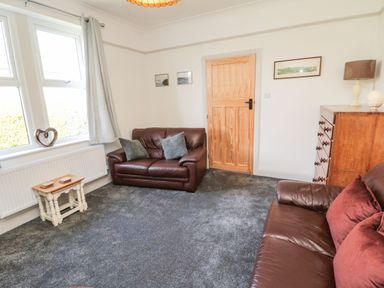 A sitting room with two leather sofas a wooden door a chest of drawers and a small table at Bisley House in Amble