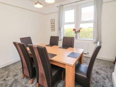 A dining room with a wooden table six chairs a window with curtains and a vase with flowers at Bisley House in Amble