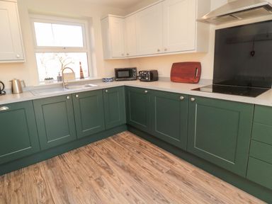 A kitchen with green lower cabinets white upper cabinets a window microwave toaster and cutting board at Bisley House in Amble