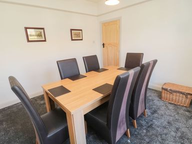 A dining room with a wooden table six black chairs two framed pictures on the wall and a wicker basket on the floor at Bisley House in Amble
