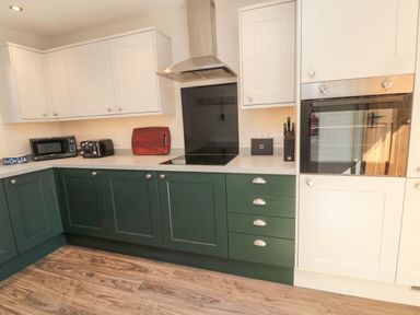 A kitchen with green lower cabinets and white upper cabinets a microwave toaster cutting board and built in oven at Bisley House in Amble