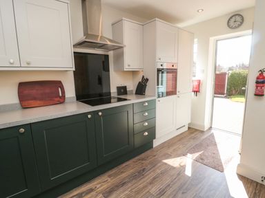 A kitchen with dark lower cabinets and light upper cabinets a stove and oven and an open door leading outside at Bisley House in Amble
