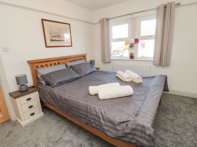 A bedroom with a wooden bed frame gray bed linens bedside tables with lamps a painting on the wall and a window with curtains and flowers on the sill at Bisley House in Amble