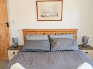A bedroom with a wooden bed frame blue pillows and a duvet two bedside tables with blue lamps and a framed painting on the wall at Bisley House in Amble